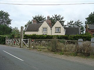 fac-on view of the station building with its two dormer windows.  At some point since conversion to a house it has been whitewashed. Just visible on the right of the house is the red brick gable of the former goods shed