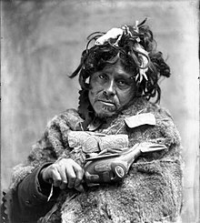 Tlingit Shaman, ca. 1900. Portrait of man wearing fur cape and carved amulet necklace, holding raven rattle Tlingit shaman 1900.jpg