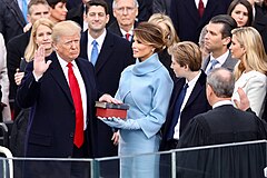 Con la mano derecha levantada, Donald Trump mira al presidente del Tribunal Supremo John Roberts de espaldas a la cámara, mientras Melania Trump y otros miran.