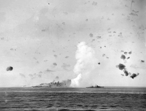 12 August 1942: Indomitable on fire after being bombed. HMS Charybdis is screening the carrier.