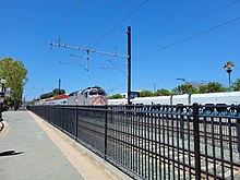 Служба Caltrain прибывает на станцию ​​Маунтин-Вью на фоне легкорельсового поезда VTA.