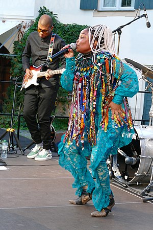 Full body picture of Nomfusi in a dancing pose, dressed in a blue African syle pant suit