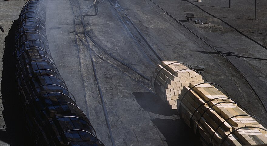 Wood railroad ties before (right) and after (left) infusion with creosote, being transported by railcar at a facility of the Santa Fe Railroad, in Albuquerque, New Mexico, in March 1943. This U.S. wartime governmental photo reports that "The steaming black ties in the [left of photo]… have just come from the retort where they have been infused with creosote for eight hours." Ties are "made of pine and fir... seasoned for eight months" [as seen in the untreated railcar load at right].[1]