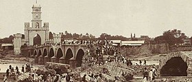 Refugees walk across a bridge with the Afzal Darwaza in the background, during the Great Musi Flood of 1908, Hyderabad.jpg