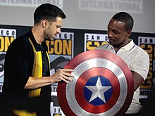 The shield, as depicted in the MCU, being held by Anthony Mackie and Sebastian Stan, who portray Sam Wilson and Bucky Barnes respectively, at the 2019 San Diego Comic-Con Sebastian Stan & Anthony Mackie (48469219356).jpg