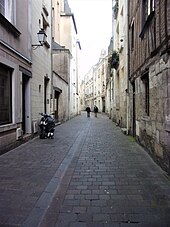 Photographie en couleurs d'une rue pavée, vue en enfilade entre deux deux rangées de façades.