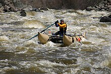 A man on a cataraft paddling through rapids of foam and green water