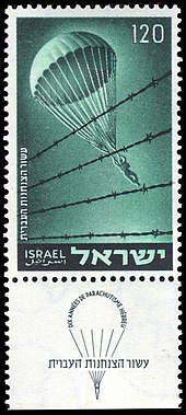 Poštovní známka znázorňující parašutistu při seskoku za ostnatým drátem