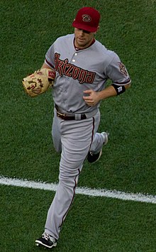 A man in a grey baseball jersey and red hat with a script 