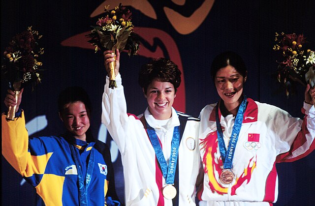 Gold medallist Nancy Johnson (centre) of the U.S., raises her hands with silver medallist Kang Cho-hyun (left), of South Korea, and bronze winner Gao 