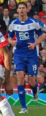 White man wearing blue and white sports clothing running.