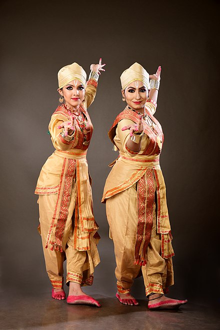 Two femaleattriya Dancers in the male sattriya costume (dhoti) and paguri (headwear) striking a pose with alapadma hastas. This pose is pefromed in the beginning of a few dance pieces which means to greet the audience sitting in front of them before starting a performance on stage.