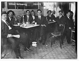 Patrons of a Syrian restaurant playing cards and smoking hookah (1910)