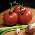 Tomatoes and other salad ingredients on wooden cutting board as an example for modern food photography: simple and natural, selective focus, shallow angle, extreme close-up.