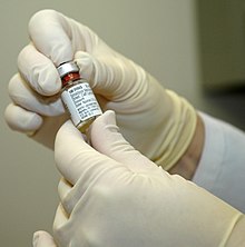 Dłoń w rękawiczce trzyma fiolkę liofilizowanej szczepionki przeciwko ospie.