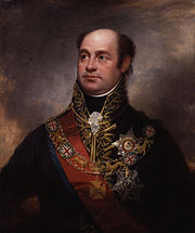 Painting shows a bald man in a high-collared dark blue military uniform with much gold braid. He wears a red sash and a number of decorations.