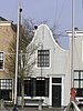 Huis met gepleisterde klokgevel. Staafankers. Voordeuromlijsting met verdiepte posten