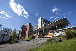 Man sieht den Eingang der Vestischen Kinder- und Jugendklinik Datteln in der Sonne. Vor der Klinik stehen zwei Rettungswagen.