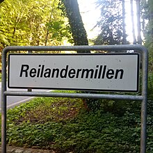 White streetsign of the lieu-dit Reuland-Moulin. Note that only the luxembourgish name is signposted. Luxembourg road sign F,14a Reilandermillen.jpg