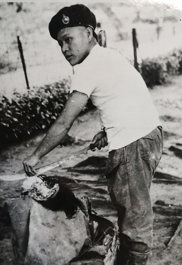 An Iban headhunter during the Malayan Emergency (1948–1960) prepares a human scalp above a container of human body parts.