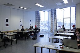 Просторный класс с учениками-подростками, работающими в пары за партами с портативными компьютерами. 