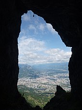 Agglomération cernée de montagnes vue « en médaillon » au travers des parois d'une grotte.