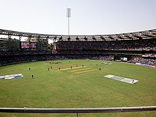 क्रिकेट मैच के दौरान क्रिकेट के मैदान का उपर से दृश्य; खिलाड़ी मैदान में दिखाई दे रहे हैं।