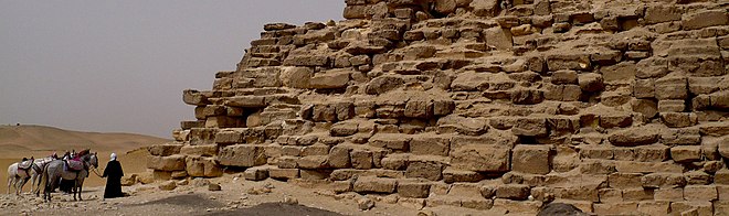 Panoramabilde ved foten av en pyramide, av rytterne sett bakfra til venstre.