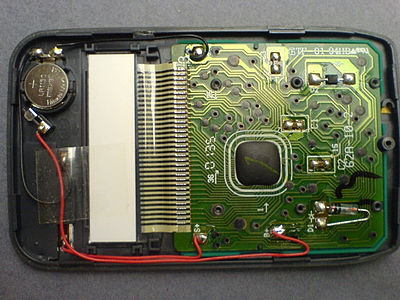 The interior of a newer (c. 2000) pocket calculator. It uses a button battery in combination with a solar cell. The processor is a "Chip on Board" type, covered with dark epoxy.