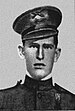 Face of a young man in military uniform. He has a stern expression and his hat, a peaked cap, is slightly cocked.