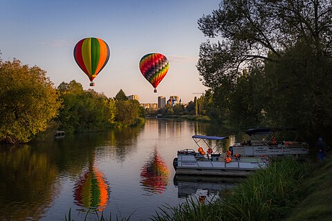 Hot air ballons fly over the river.