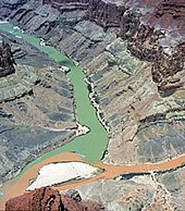 The Little Colorado River (right)'s confluence with the Colorado River (center). Note that the Little Colorado is a light brown color caused by recent cloudbursts, while the Colorado is an emerald green. When Powell and his crew arrived here in 1869, it was this color of the river that they saw, while the Colorado's green color is caused by Glen Canyon Dam trapping sediment.