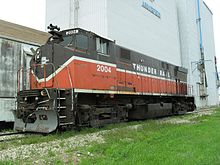 A diesel locomotive parked on a railroad track in front of an industrial building. It is number 2004, and says "THUNDER RAIL" on its side. The paint scheme is unmistakably that of the Providence and Worcester Railroad, with P&W's red on the bottom portion and brown on the top, separated by a white line, which dips down and then back up on the front of the locomotive.