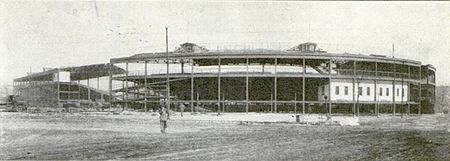 Cubs Park grandstand, seen in January 1923 from the corner of Clark and Addison, divided into three segments during the 1922-23 expansion, prior to the construction of additional sections between the relocated segments. Note that, in the days before the famous marquee was installed, the ballpark was identified by a sign along the top of the grandstand reading "Chicago National League Baseball Club". Relocation of Cubs Park grandstand 1922-23.jpg