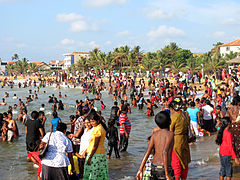 A crowded beach, with many people going into the water with their clothes on