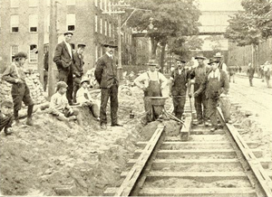 Railway workers and George Pellissier (center left) stand next to a thermite crucible prior to ignition during the laying of the first tracks in the United States using the thermite weld technique, August 1904 Street railway workers with a thermite crucible on Main Street, Holyoke, 1904.png