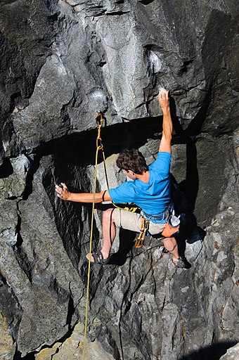 Man sport climbing under overhang