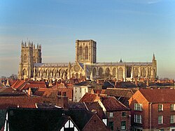 York Minster seen from the side – a long building with a pair of towers at one end and a massive central tower with two perpendicular windows. The round rose window can be seen on the south transept.
