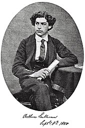Sullivan sentado con una pierna cruzada sobre la otra, de 16 años, con su uniforme de la Royal Academy of Music, mostrando su cabello espeso y rizado.  En blanco y negro.