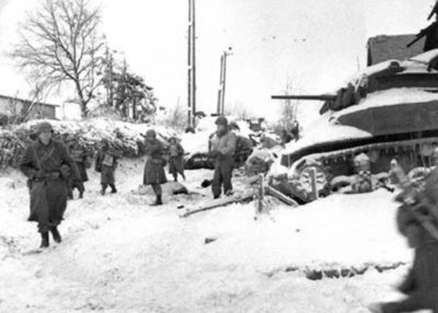 Men of the 117th Infantry Regiment, part of the 30th Infantry Division, move past a destroyed American M5 "Stuart" tank on their march to capture the 