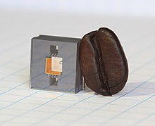 The heart of NIST's next-generation miniature atomic clock - ticking at high "optical" frequencies - is this vapor cell on a chip, shown next to a coffee bean for scale. 18pml015 clock-chip-with-coffee-bean 2mb.jpg