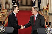 Tony Blair i George W. Bush ściskają dłonie na konferencji prasowej.