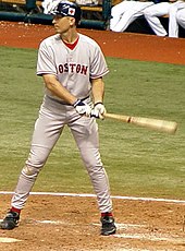 A man wearing a gray baseball uniform and navy-blue baseball helmet swinging a baseball bat