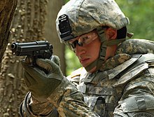 A United States Army soldier in 2009 demonstrates the usage of his Beretta M9 sidearm. M9 Pistol combat in woods.jpg