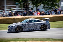 Voiture blanche aux motifs noirs, vue de profil, sur une piste, devant une foule.