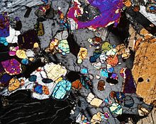 Photomicrograph of a thin section showing the strong presence of olivine (brightly colored, rounded grains) surrounded by plagioclase and pyroxene grains within the olivine-rich zone. Crossed polars, 40x Palisades Sill Olivine Zone.jpg