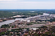 Aerial view of an industrial zone; large silos, cranes, storage tanks, and a highway are seen.