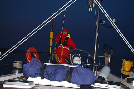 Eine Seglerin am Steuer während einer Nachtfahrt, mit Rettungsweste und Lifebelt