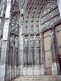 Photo : ébrasement du portail, le Christ sur le trumeau (à droite) ; dans les niches, les apôtres et premiers diacres.