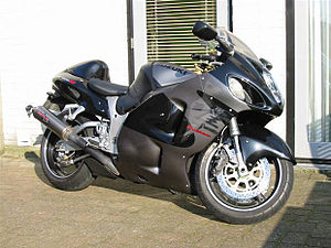 A modern sport motorcycle with enclosed black and gray bodywork leaning on its sidestand on smooth paving stones in front of a white wall